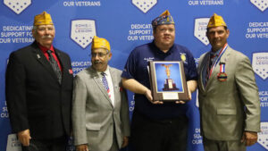 Four men stand side by side. One holds a plaque.