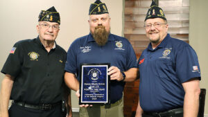 3 men stand side by side. The center one holds a plaque.